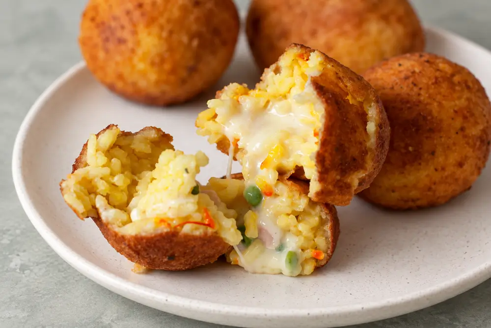 Fried rice balls cut open to show melted cheese, ham and peas inside.