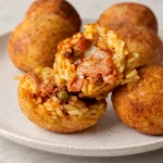 Fried Arancine cut open to show the ragù, peas and melted cheese filling.