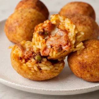Fried Arancine cut open to show the ragù, peas and melted cheese filling.