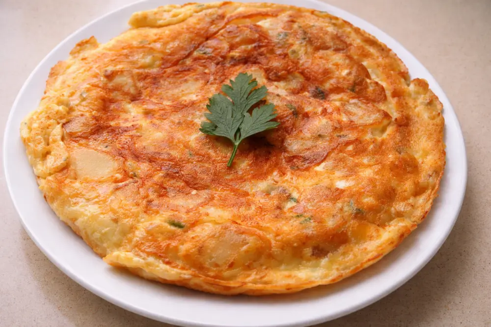 Frittata con le patate served on a plate with a lightly crisp golden surface and parsley on top.