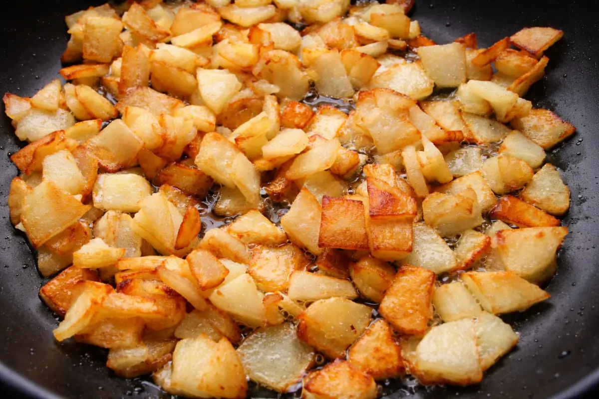 Diced potatoes frying in oil until lightly golden with crisp edges forming.