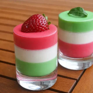 Panna Cotta Tricolore served in small glasses with strawberry and mint garnishes.