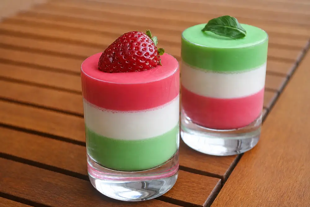 Panna Cotta Tricolore served in small glasses with strawberry and mint garnishes.