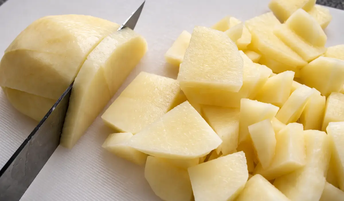 Peeled potatoes being cut into small pieces on a chopping board.