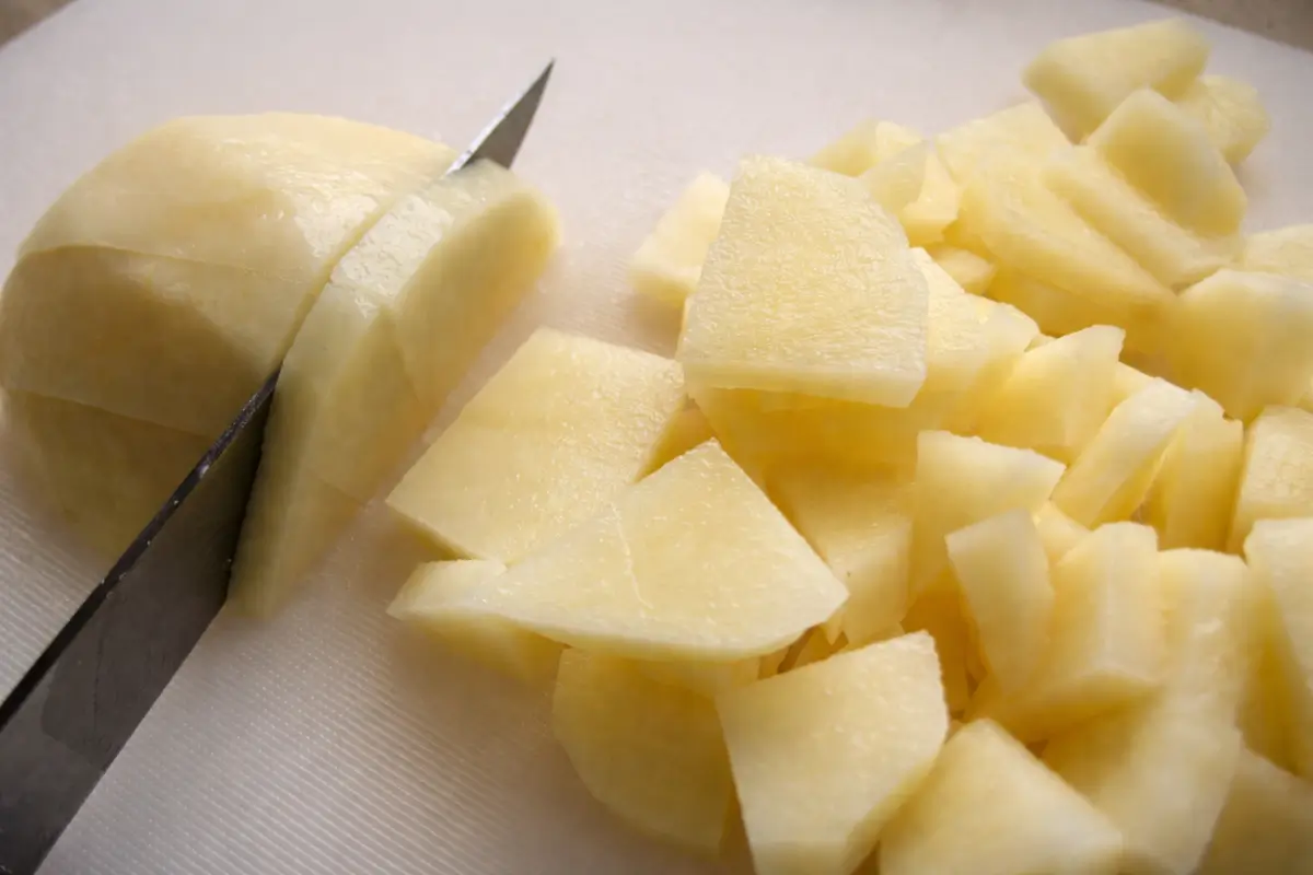 Raw potatoes being sliced into small pieces on a cutting board.