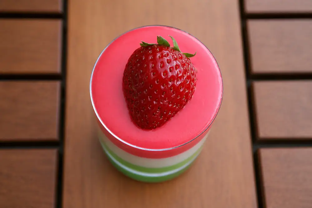 Layered panna cotta topped with a glossy fresh strawberry.