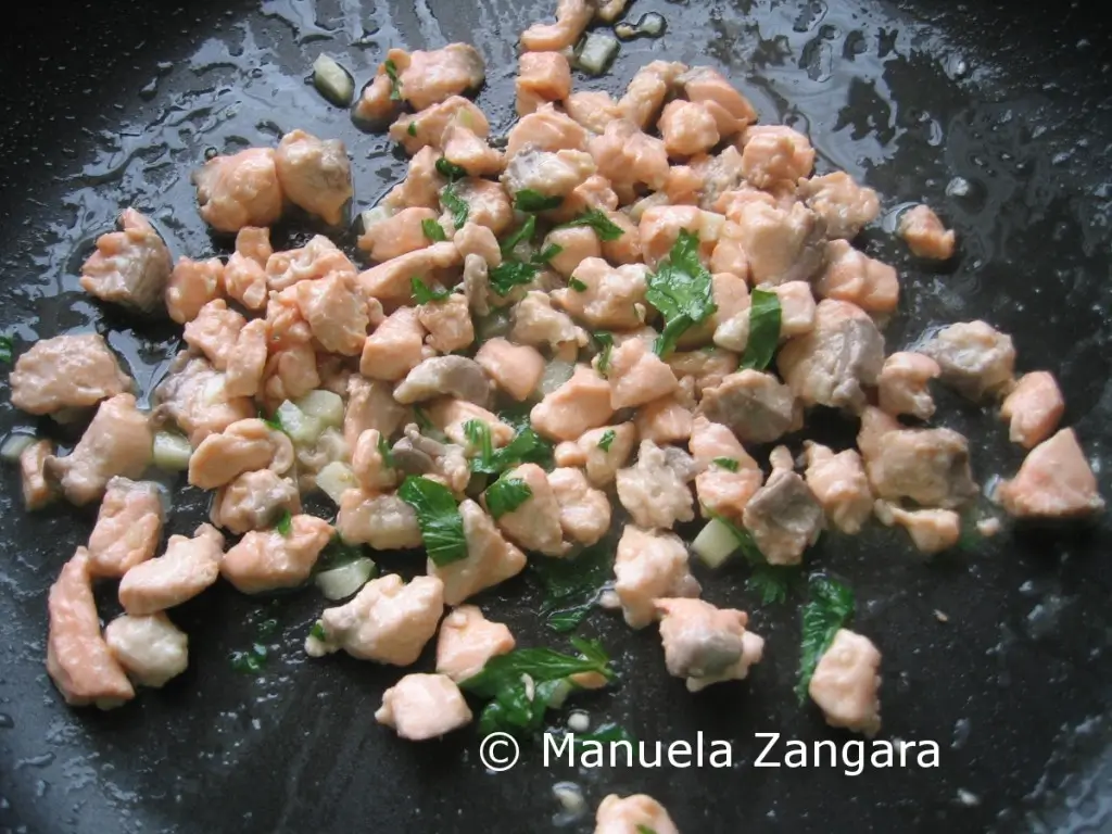 Salmon cooking with garlic and parsley in a frying pan.