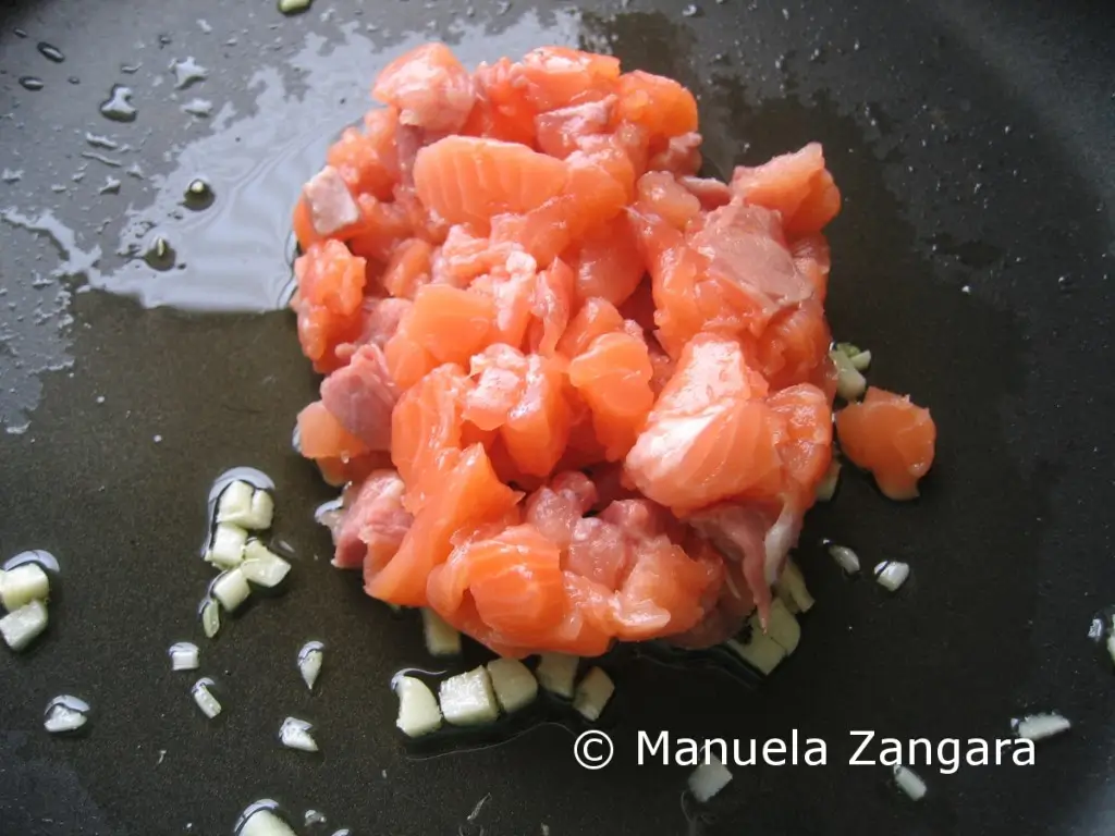 Salmon pieces cooking with garlic and olive oil.