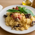 Couscous Salad served on a white plate and garnished with fresh basil leaves.