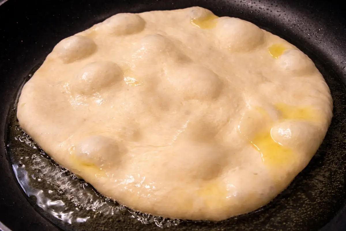 Pizza dough frying in hot oil with air bubbles forming on the surface.