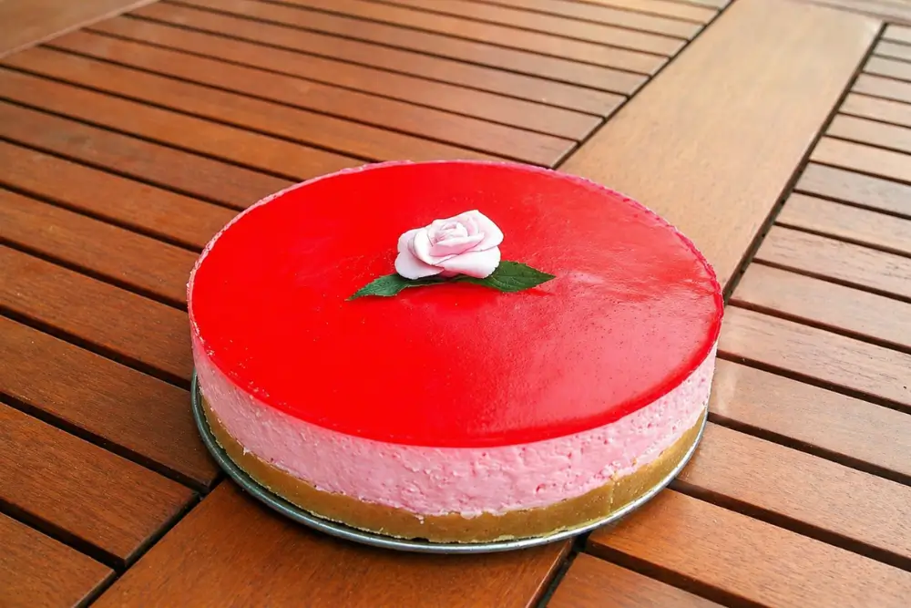 Whole no-bake cheesecake with glossy rose topping and fondant rose decoration.