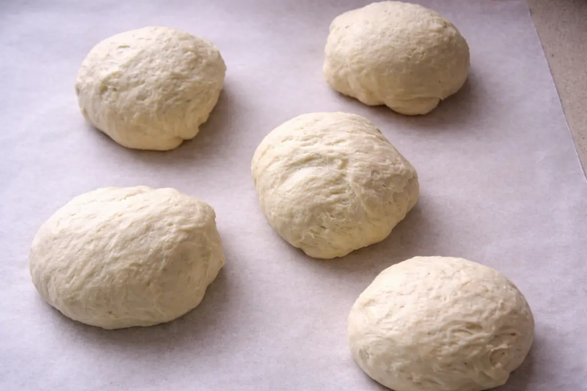 Soft pizza dough balls resting on baking paper before shaping.