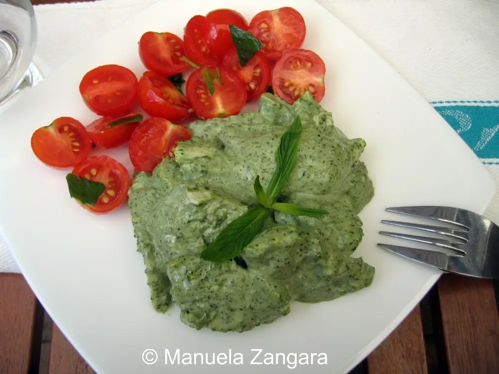 Poached chicken with mint sauce served with cherry tomatoes on a plate.
