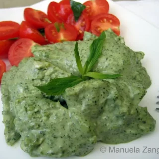 Close-up of poached chicken in creamy mint sauce with cherry tomatoes on a white plate.
