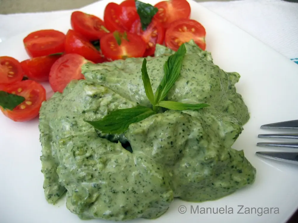 Close-up of poached chicken in creamy mint sauce with cherry tomatoes on a white plate.
