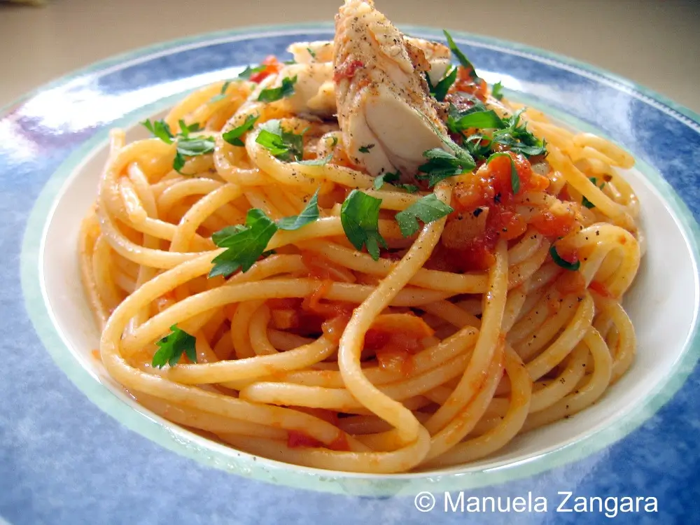 Close-up of spaghetti coated in tomato sauce with pieces of cooked fish and parsley.