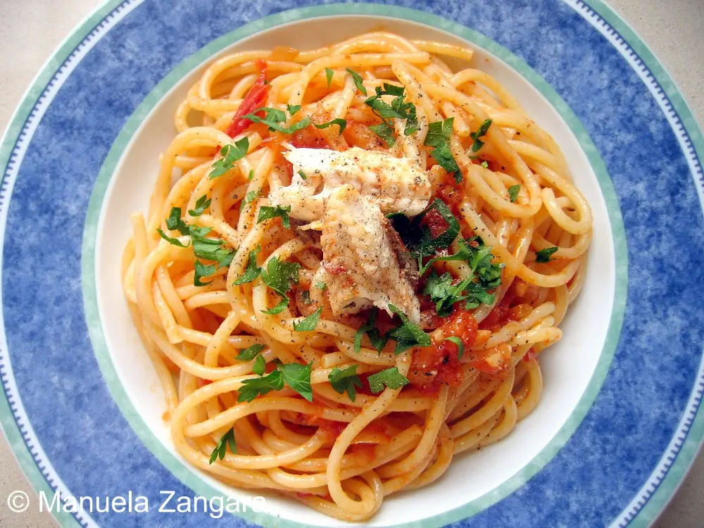 Overhead shot of plated spaghetti with tomato sauce, cooked fish, pepper, and parsley.