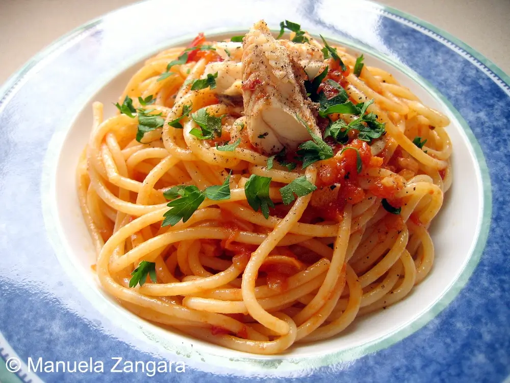 Plate of spaghetti topped with fish flakes, tomato sauce, and parsley.