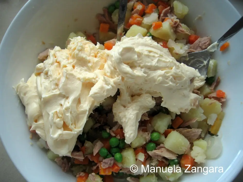 Large spoonfuls of mayonnaise added to chopped vegetables and tuna for Russian salad with tuna.