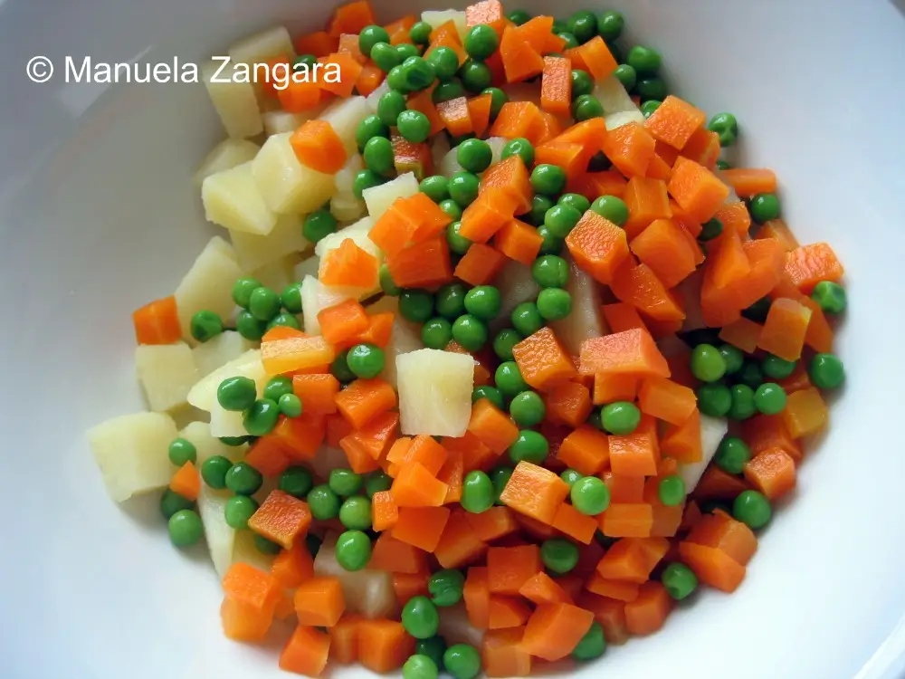 Bowl of boiled potatoes, carrots, and peas cooling after cooking.