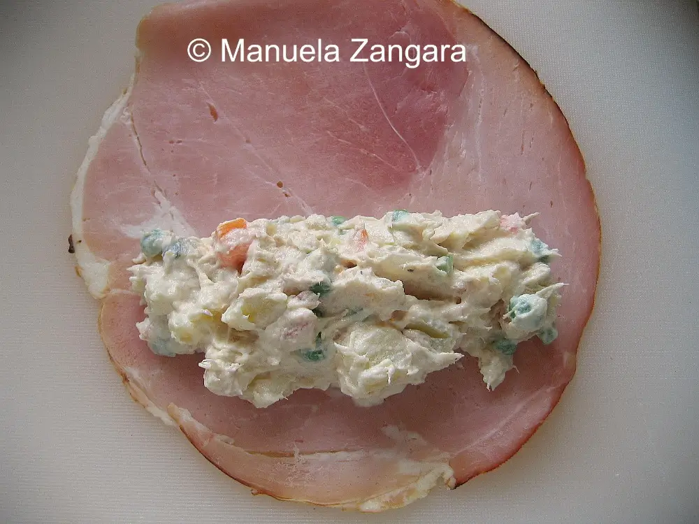Spoonful of Russian salad with ham placed on a slice of ham ready to roll.