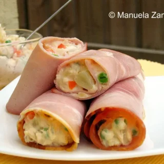 Close-up of Russian Salad wrapped in ham slices and served on a white plate.