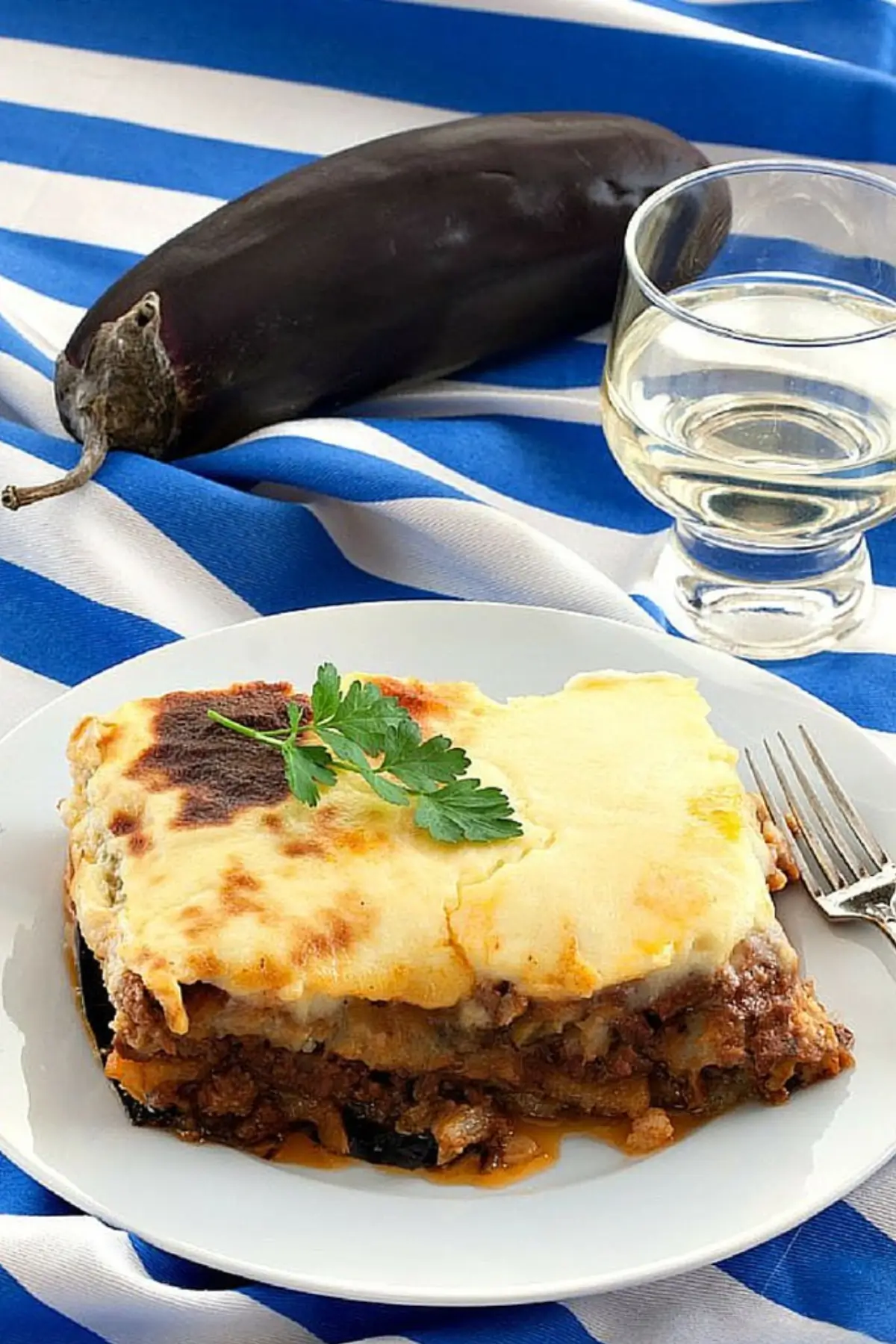 Moussaka served on a plate with golden topping and a glass of wine nearby.