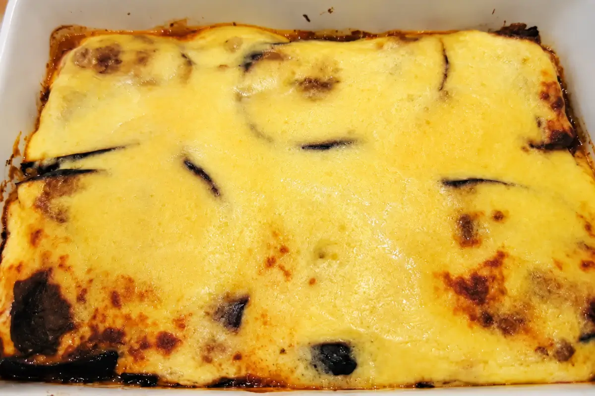 Moussaka baked in a white casserole dish with a golden béchamel topping.