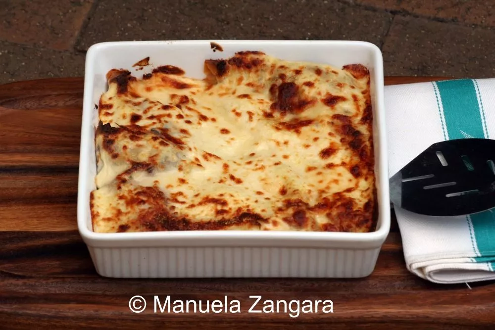 Freshly baked stuffed crespelle in a white dish with golden béchamel top.