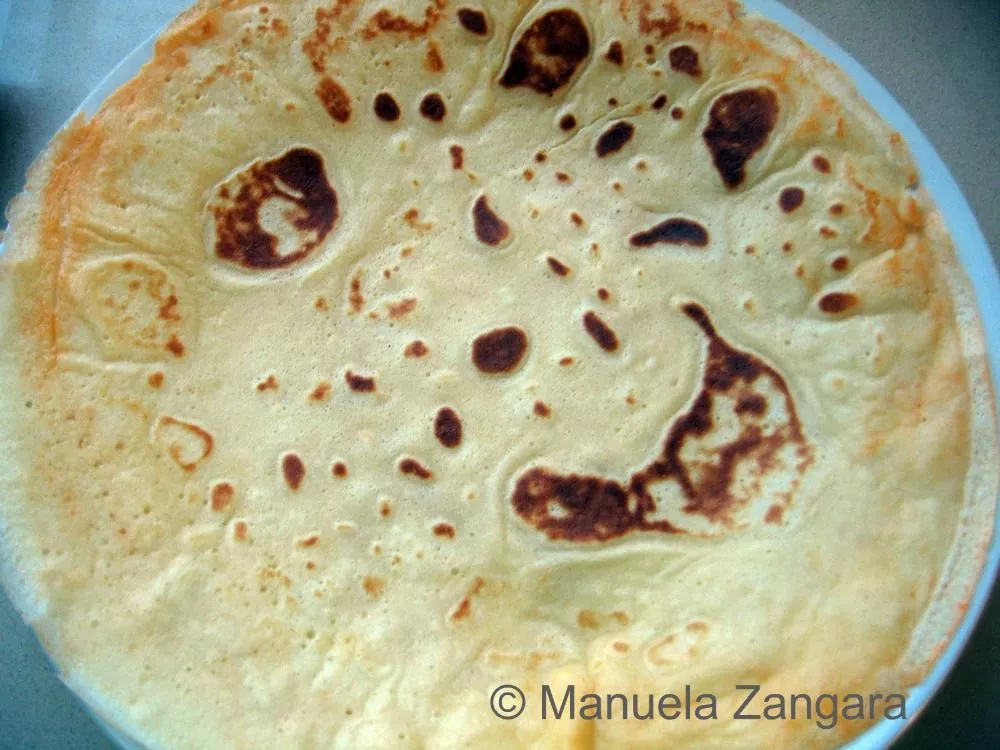 A freshly cooked crespella with light golden spots on a plate.