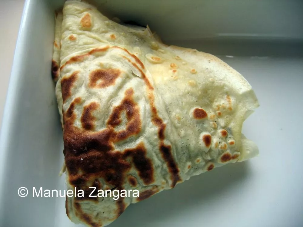 Folded crespella placed in a baking dish before adding béchamel.