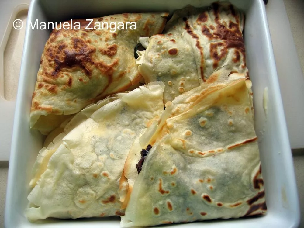 Folded crespelle arranged in a baking dish.