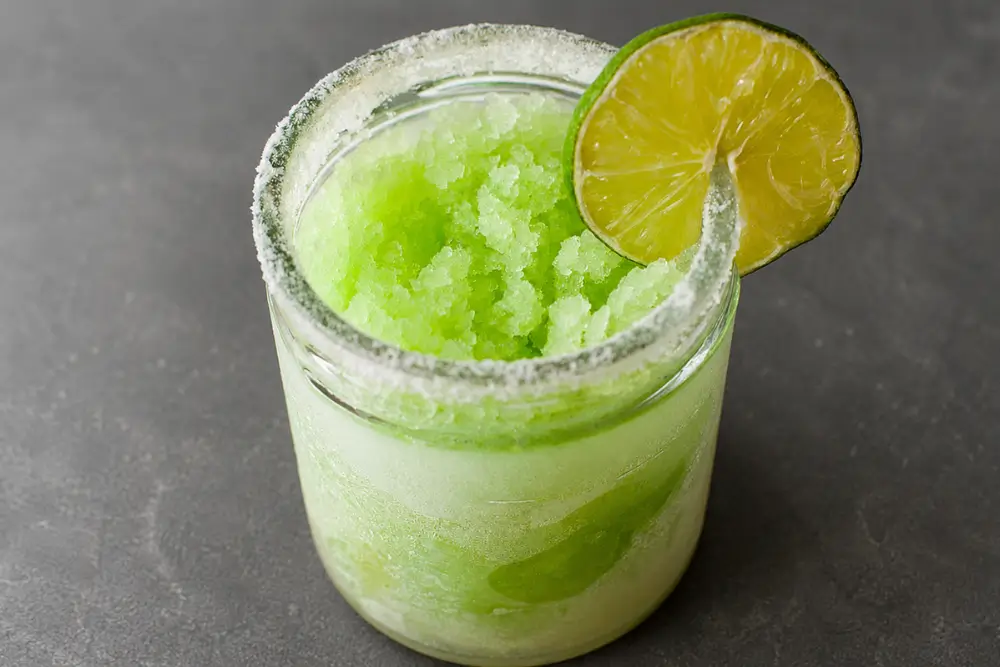Close-up of a frozen lime margarita showing its icy texture, salted rim and fresh lime garnish.