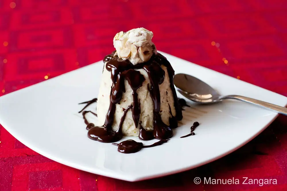 Individual semifreddo served with warm chocolate sauce and torrone pieces.