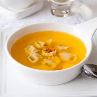 Chicken consommé with saffron served with tortellini in a white bowl.