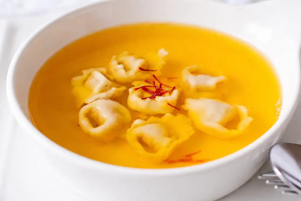 Clear chicken broth with saffron and tortellini ready to serve.