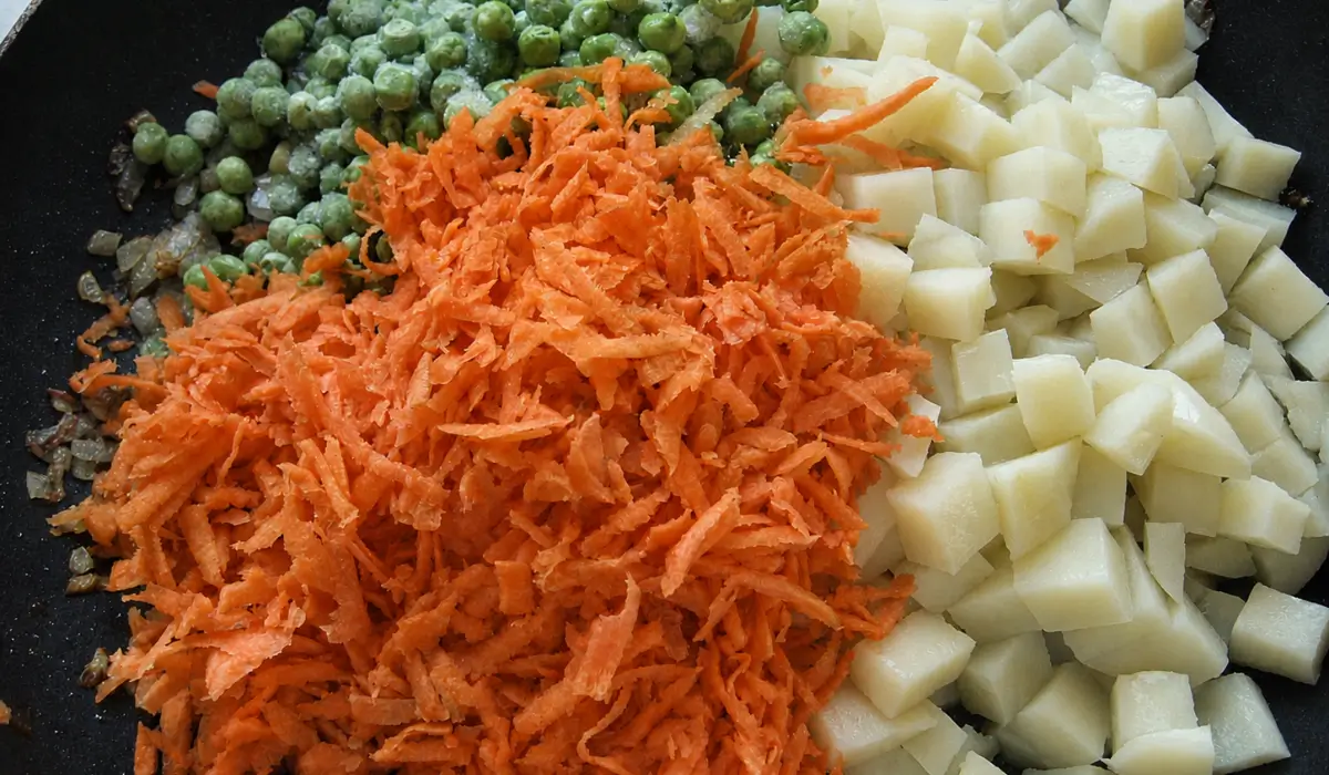 Potato, carrot, and pea filling cooking with curry spices in a frying pan.