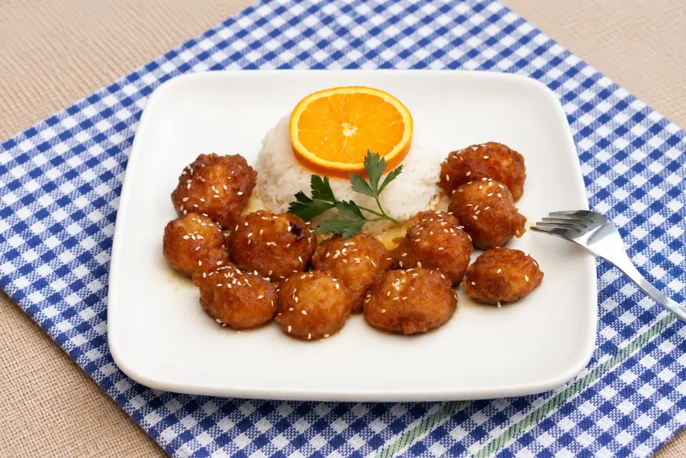 Crispy chicken coated in orange sauce served with rice and a fresh orange garnish.