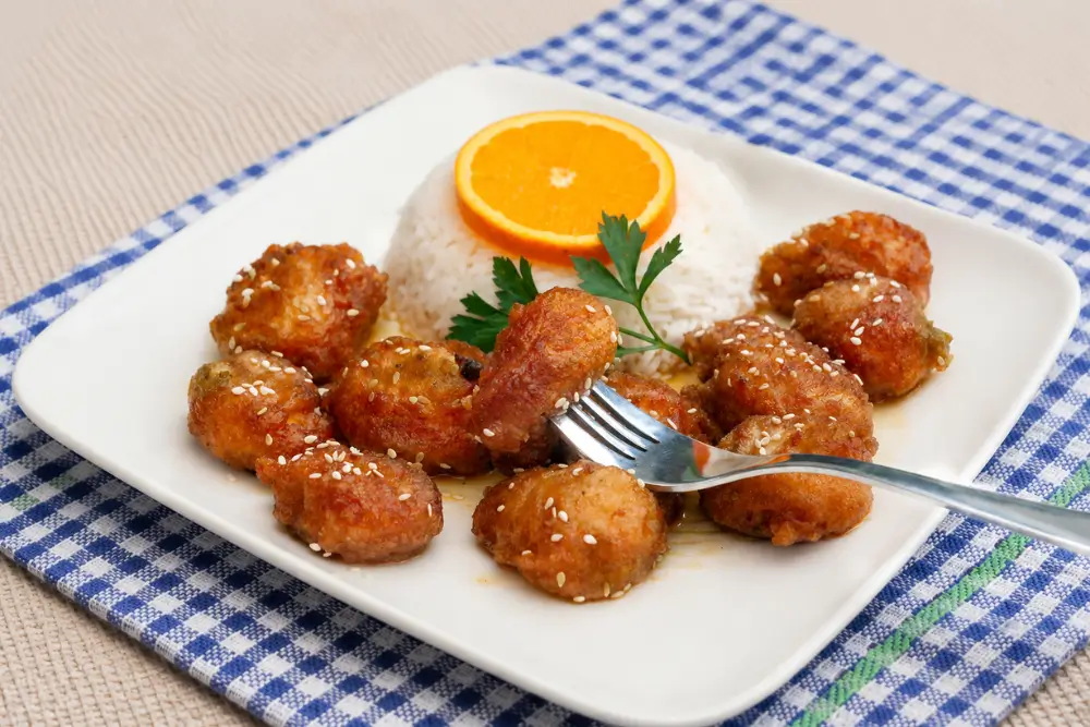 Homemade Orange Chicken served with steamed rice, sesame seeds, and an orange slice garnish.