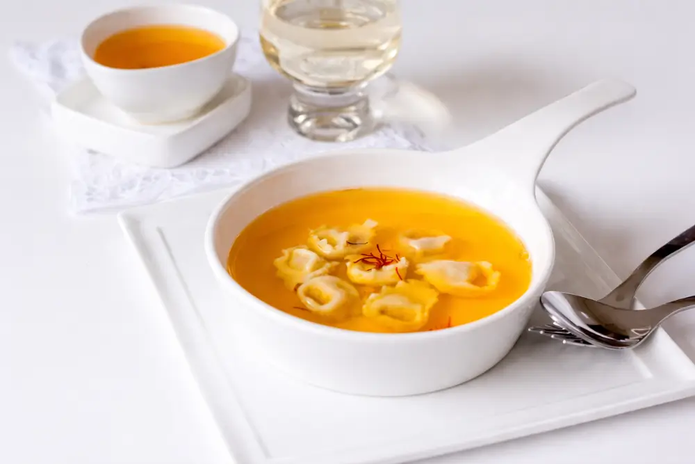 Chicken consommé plated with tortellini and served with a glass of white wine.