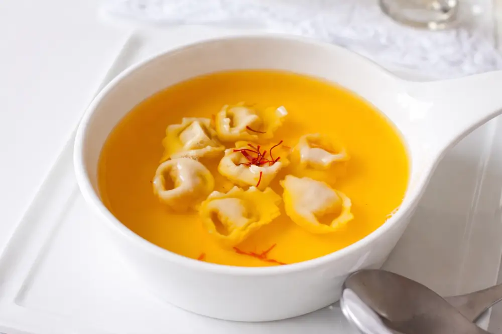 Golden saffron broth with tortellini served in a shallow white dish.