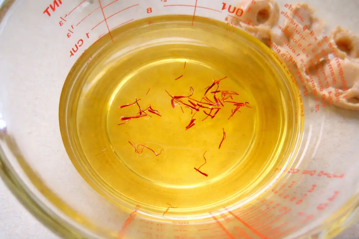Saffron threads steeping in warm consommé inside a measuring jug.