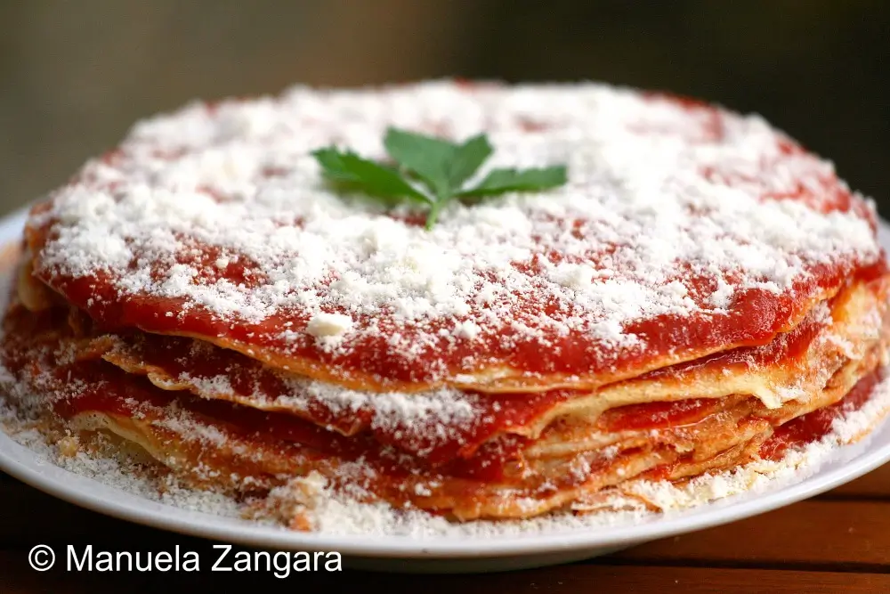 Layered frittatine stacked with tomato sauce and grated Parmigiano on a white plate.