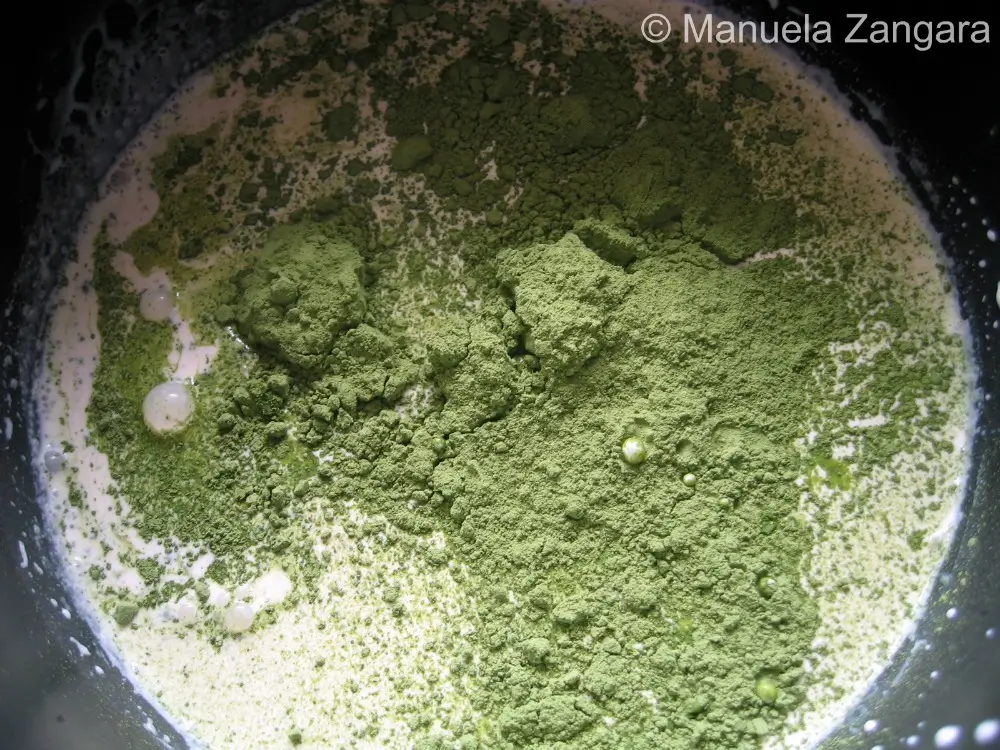 Bright green matcha powder scattered over cream and milk in saucepan.