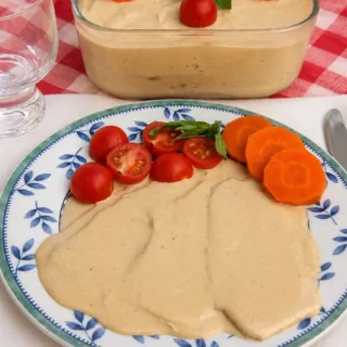 Plate of Vitello Tonnato served with cherry tomatoes, basil, and sliced carrot.