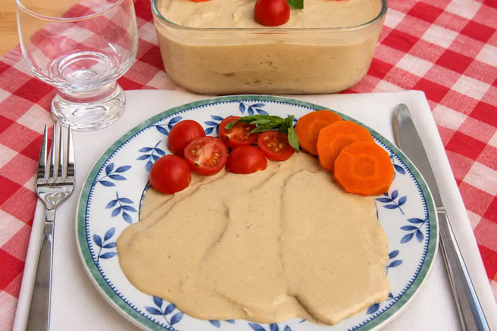 Plate of Vitello Tonnato served with cherry tomatoes, basil, and sliced carrot.