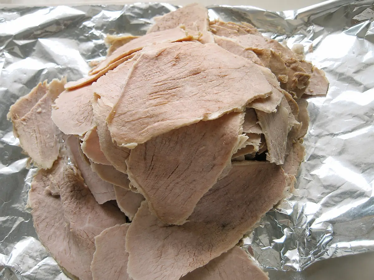 Thin slices of cooked veal prepared for assembling Vitello Tonnato.