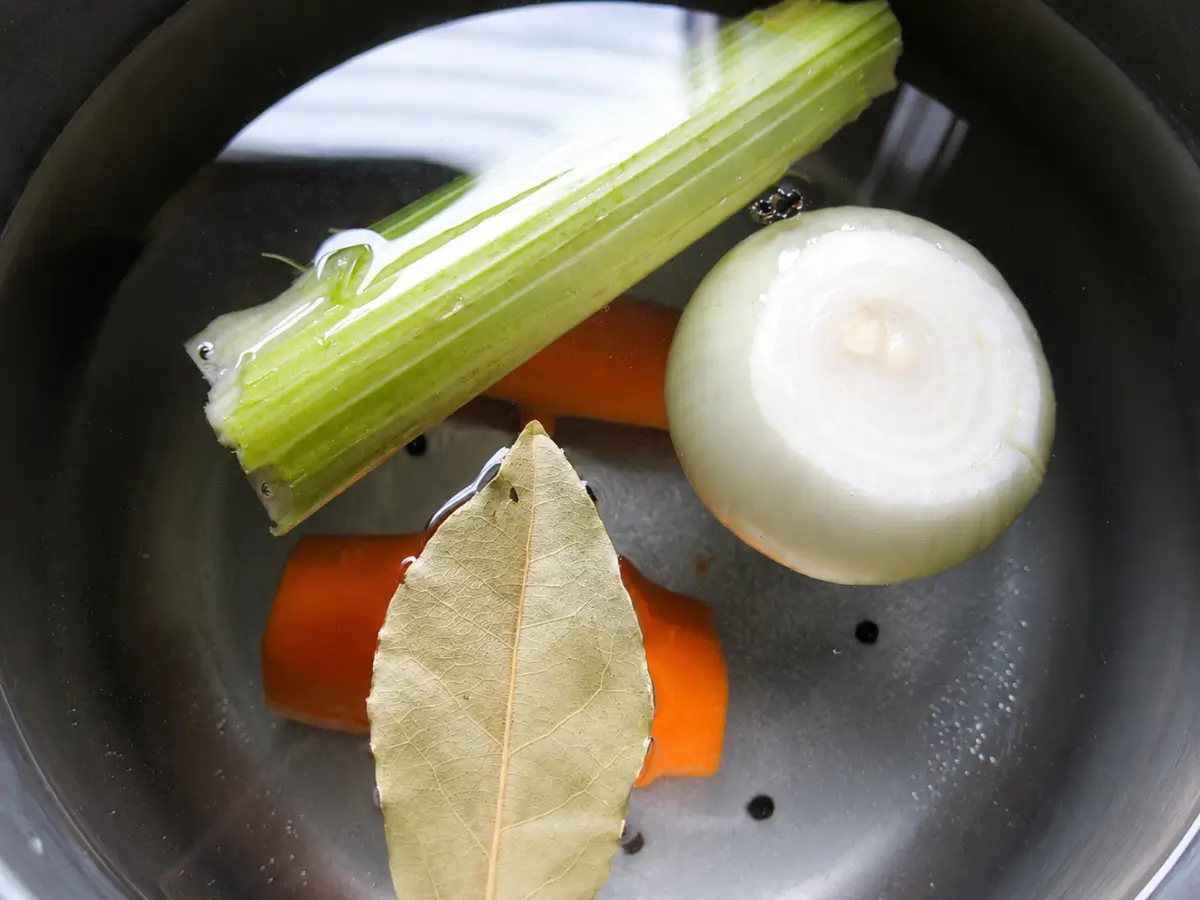 Onion, celery, carrot, bay leaf, and pepper corns prepared in water for cooking the veal.