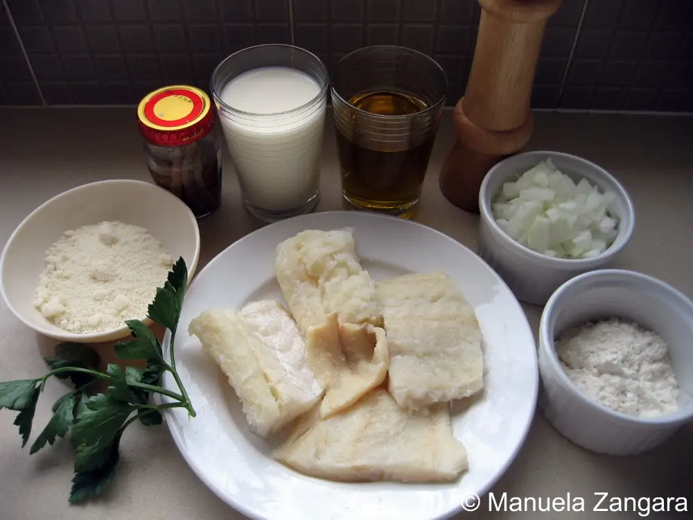 Ingredients laid out for Baccalà alla Vicentina: fish, milk, oil, cheese, onion, flour, anchovies, parsley.