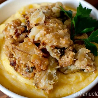 Bowl of Baccalà alla Vicentina served over soft polenta with parsley on top.